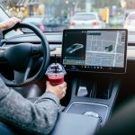 Rear view of unrecognizable female driving modern electric car. Tesla tablet screen.