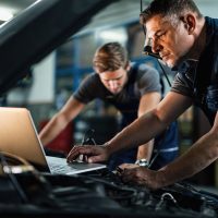 Mid adult mechanic using computer and doing car diagnostic with his coworker in auto repair shop.